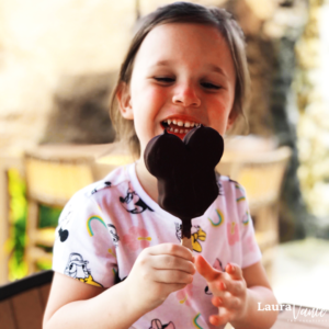 girl eats a Mickey bar to cool off at Disney World